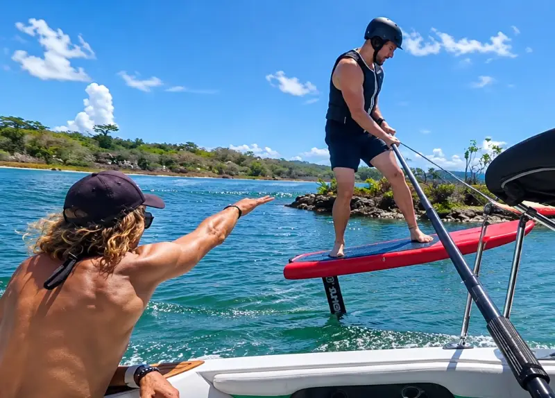 Instructor on the boat guiding a rider learning to hydrofoil behind the boat
